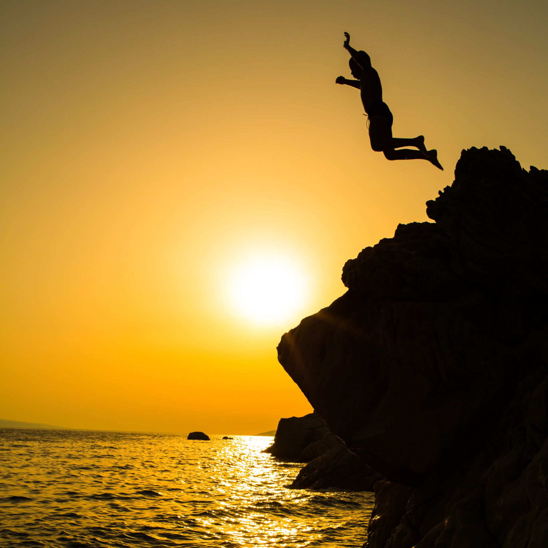Jumping in the ocean from a cliff at sunset.